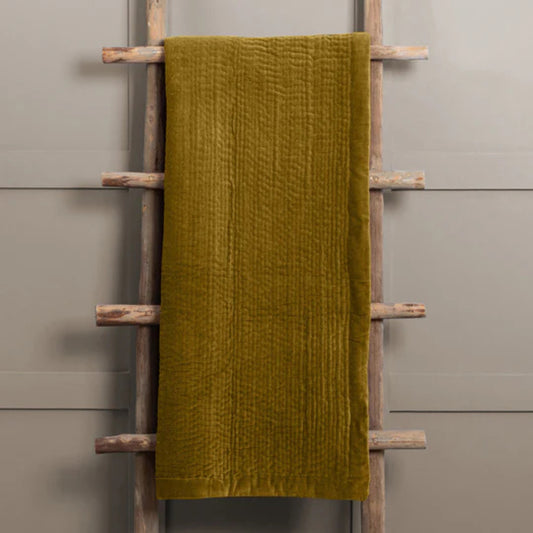 Deep mustard velvet throw draped over a wooden ladder against a gray wall