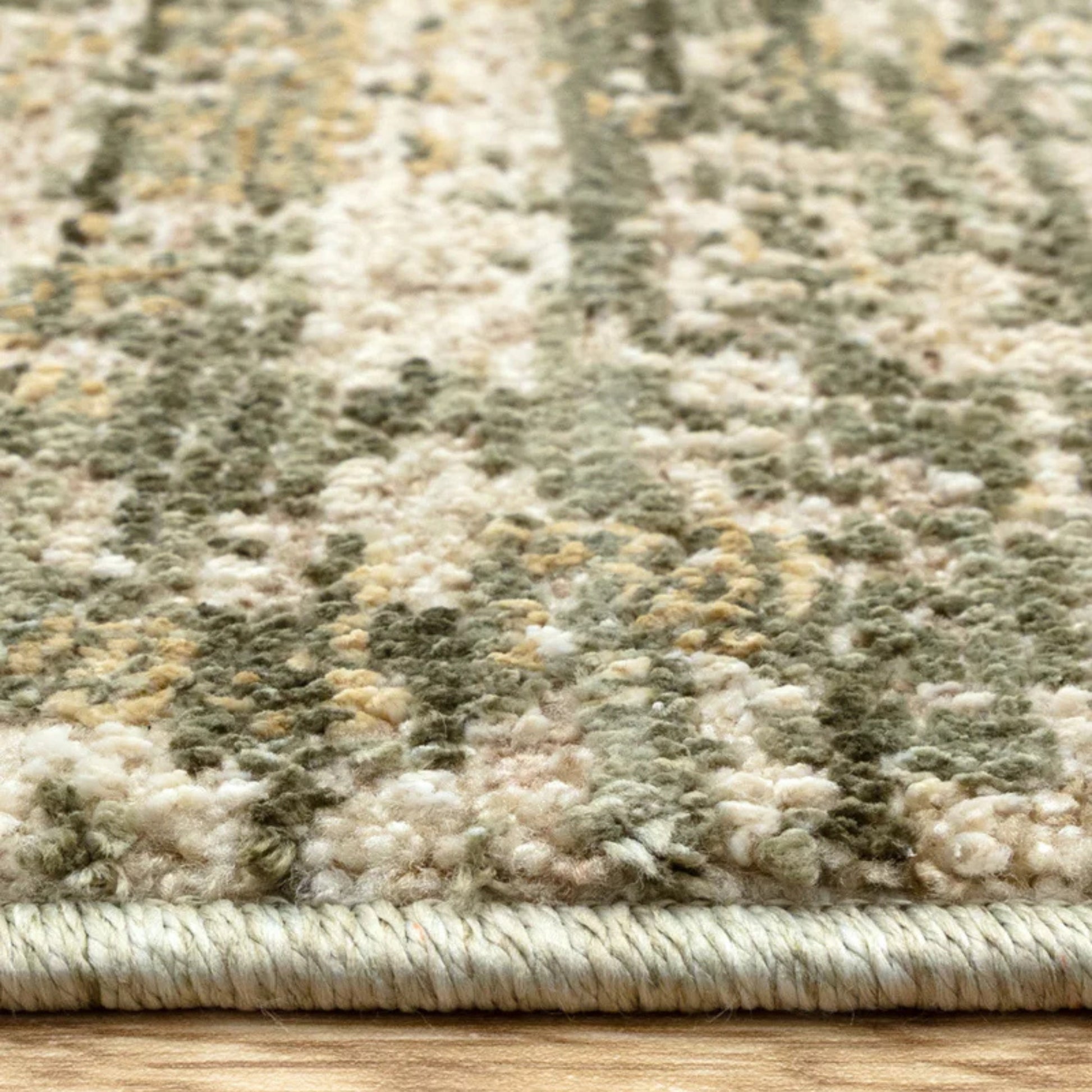 Close-up of a textured green and beige rug on a wooden floor.