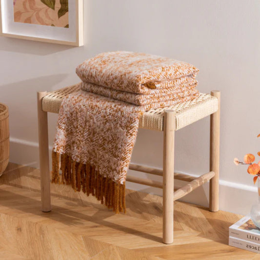 Folded throw blanket on a woven stool with a neutral background