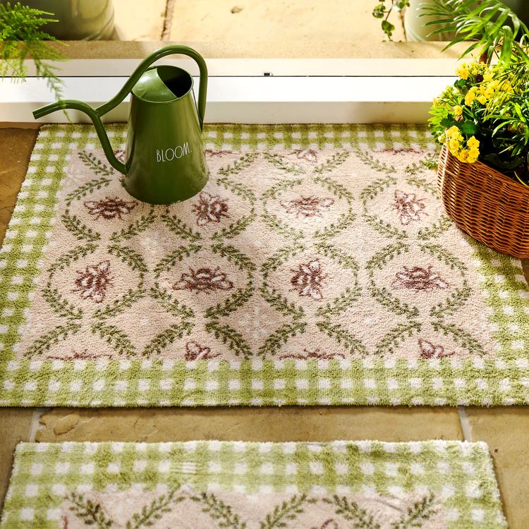 Hug Rug Bee design washable doormat at doorway entrance with green water can and basket of yellow flowers