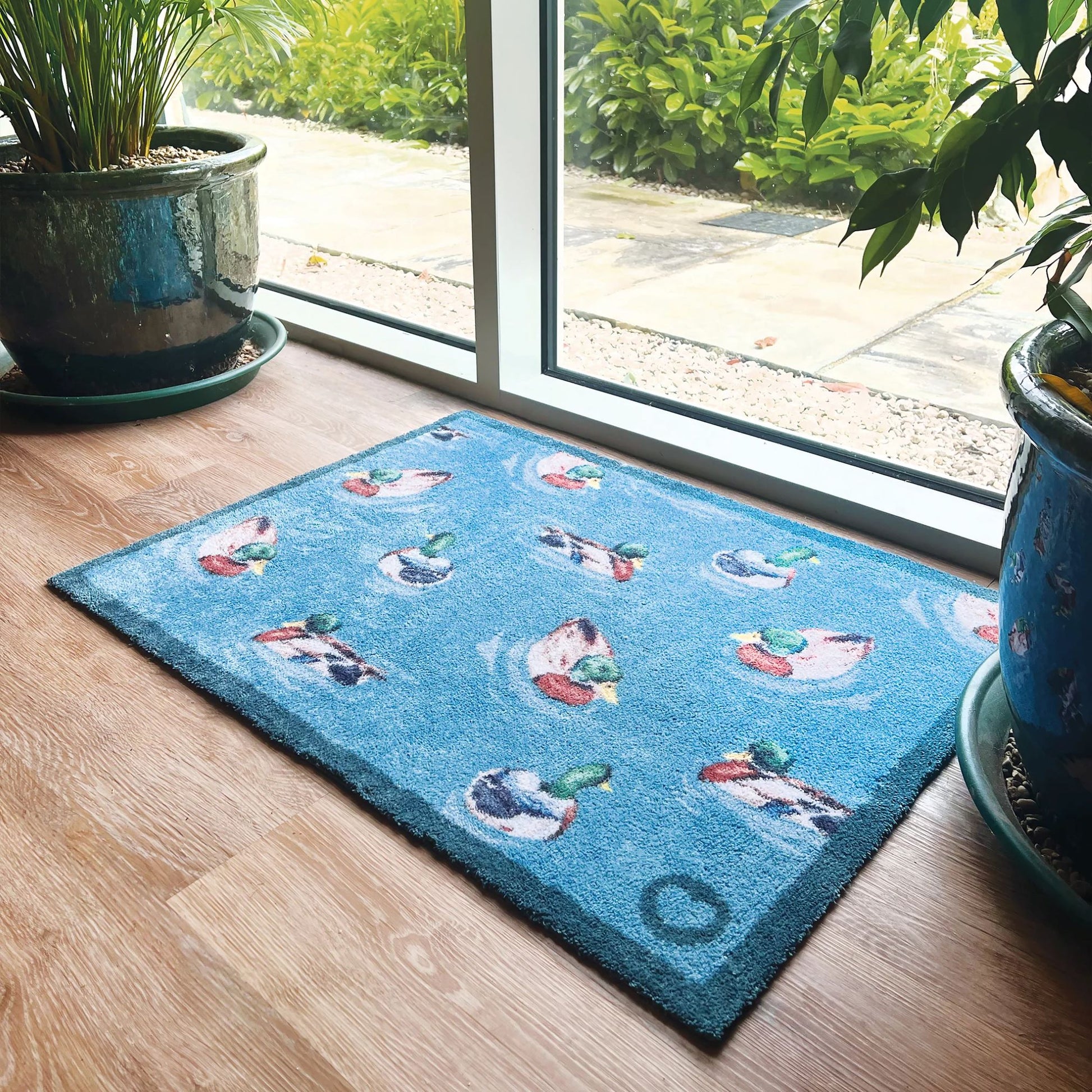 Hug Rug mat at patio door featuring swimming ducks on a blue background with two large blue plant pots either side. 