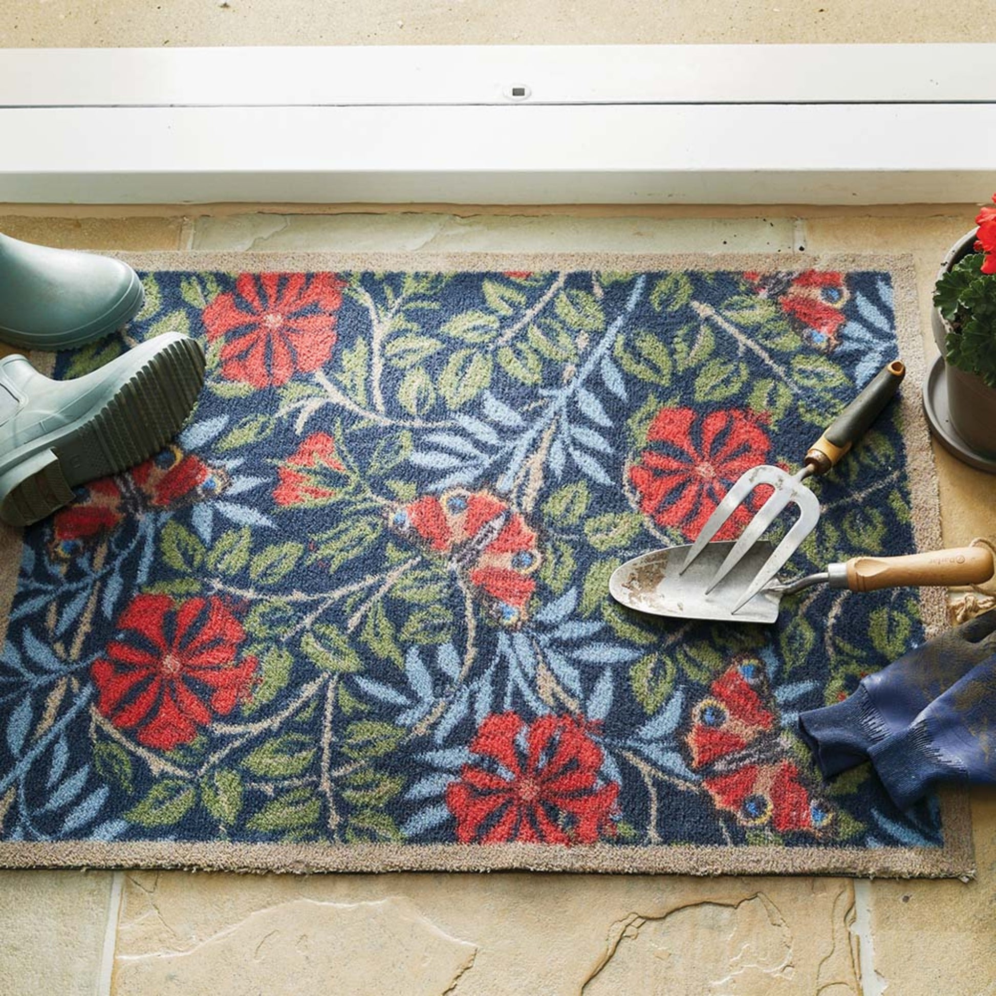 Floral patterned doormat with gardening tools and boots on a stone floor.