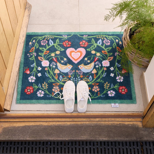 Decorative doormat with floral and heart design on a wooden floor.