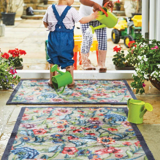 Kids with watering cans at entrance ay with 2 hug rug floral design mats and potted plants 