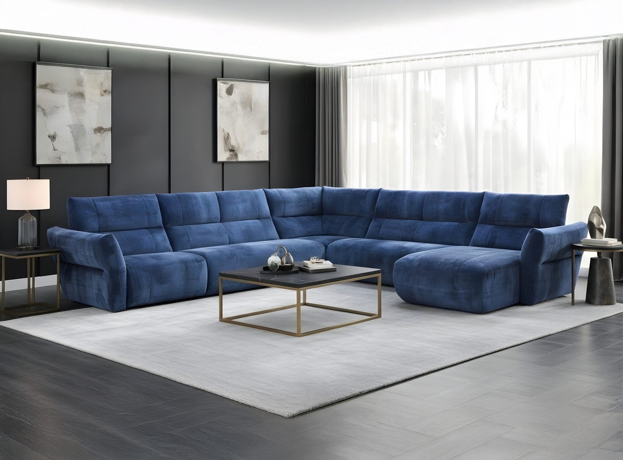 A modern sectional sofa in a deep blue velvet fabric, arranged in an L-shape with a chaise lounge on the right, set in a contemporary living room with a light gray rug, a black coffee table with gold legs, and dark gray accent walls.
