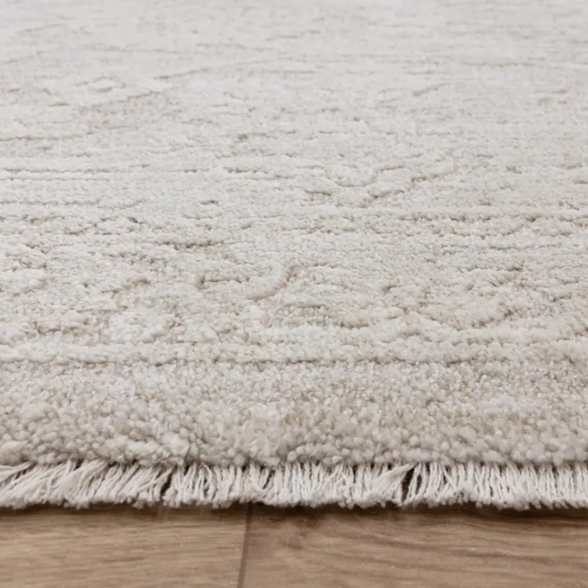 Close-up of a textured beige rug on wooden flooring.