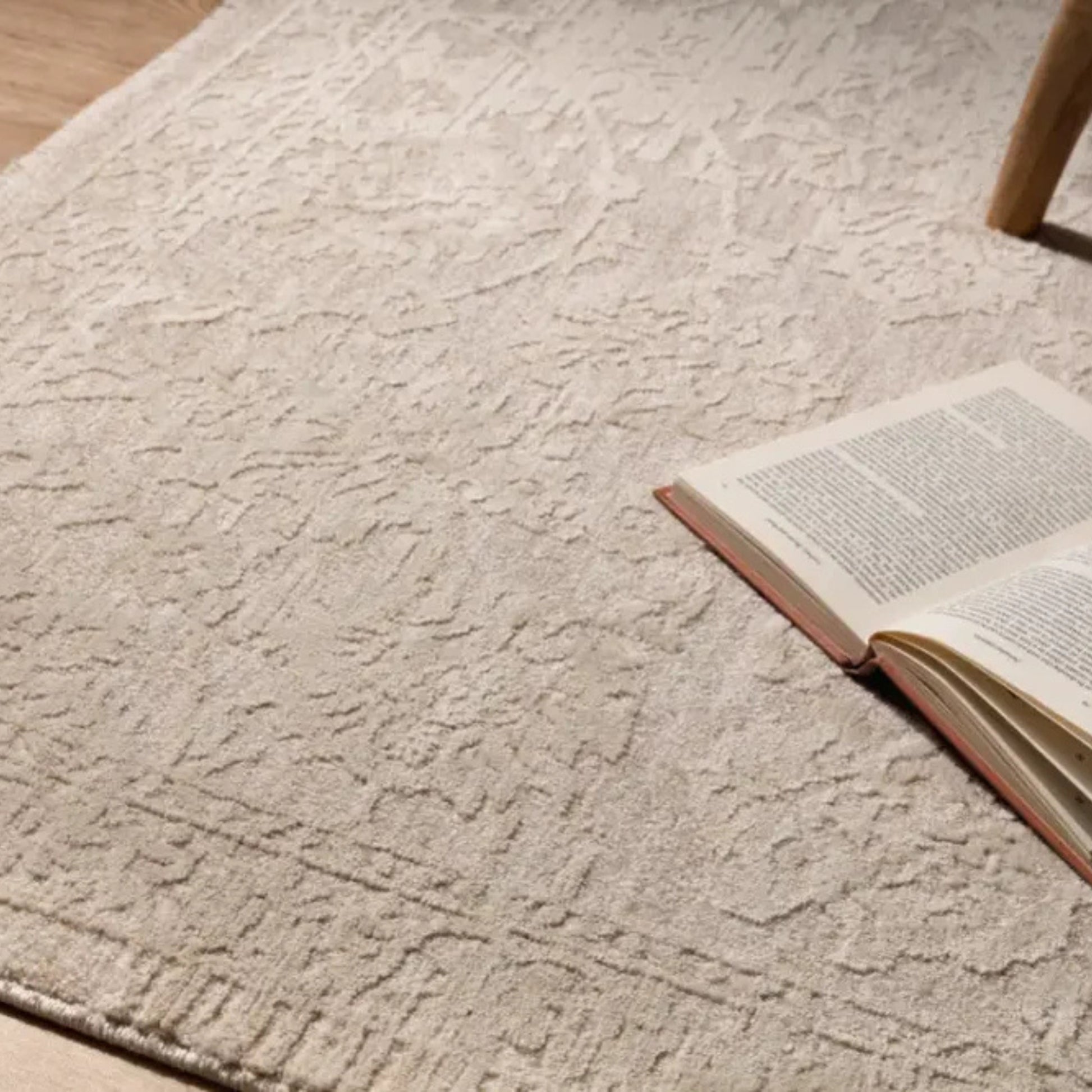 Textured beige rug with an open book on a wooden chair leg.
