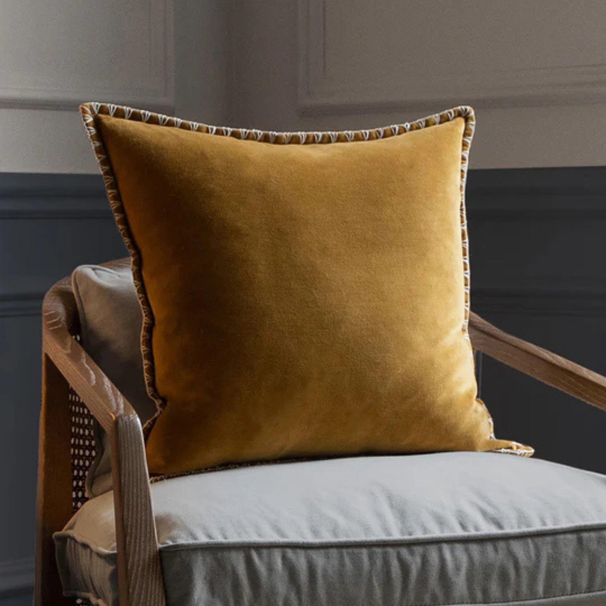 Mustard yellow pillow on a gray cushioned chair against a gray wall.