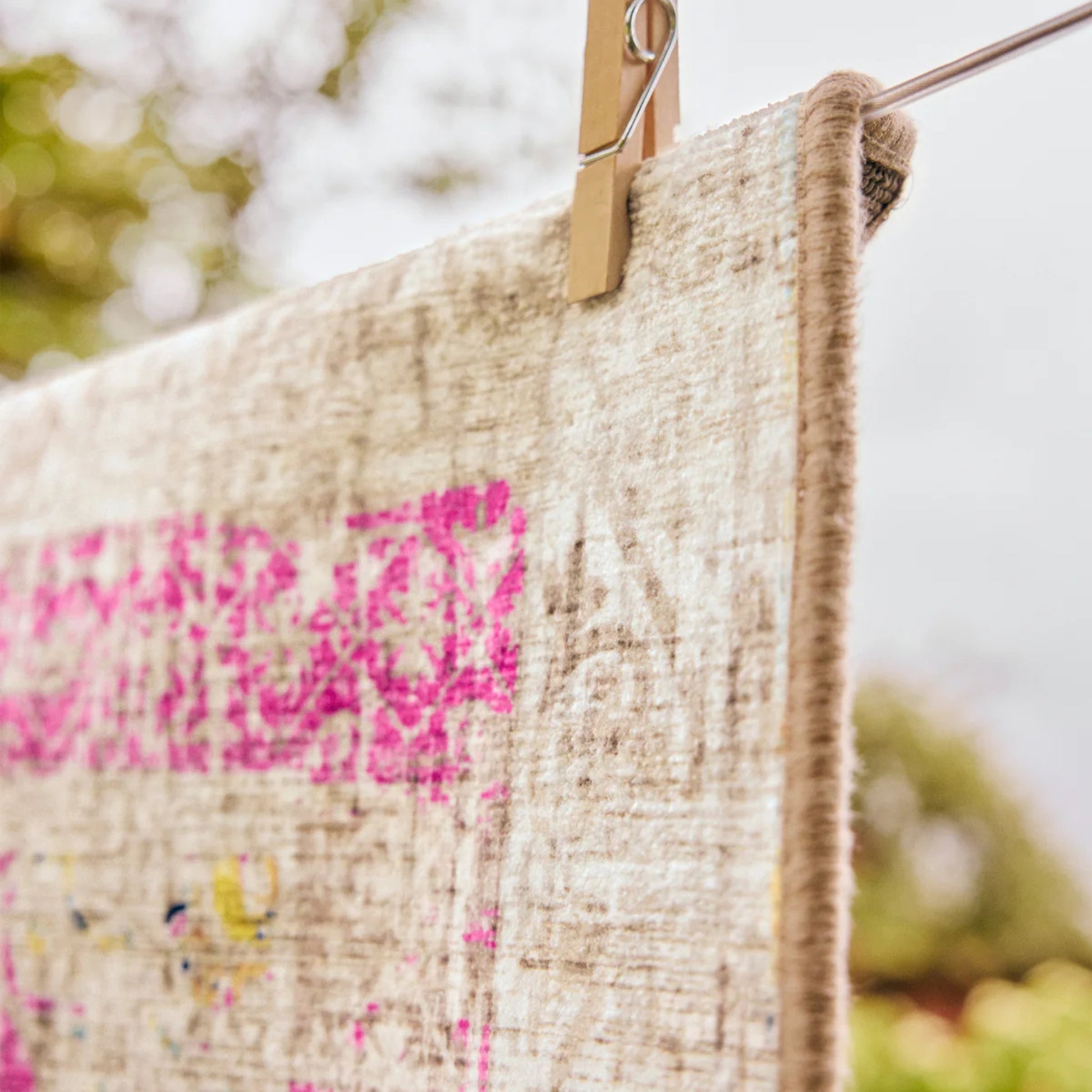 Textile with pink and multicolor patterns hanging on a clothesline with a blurred natural background