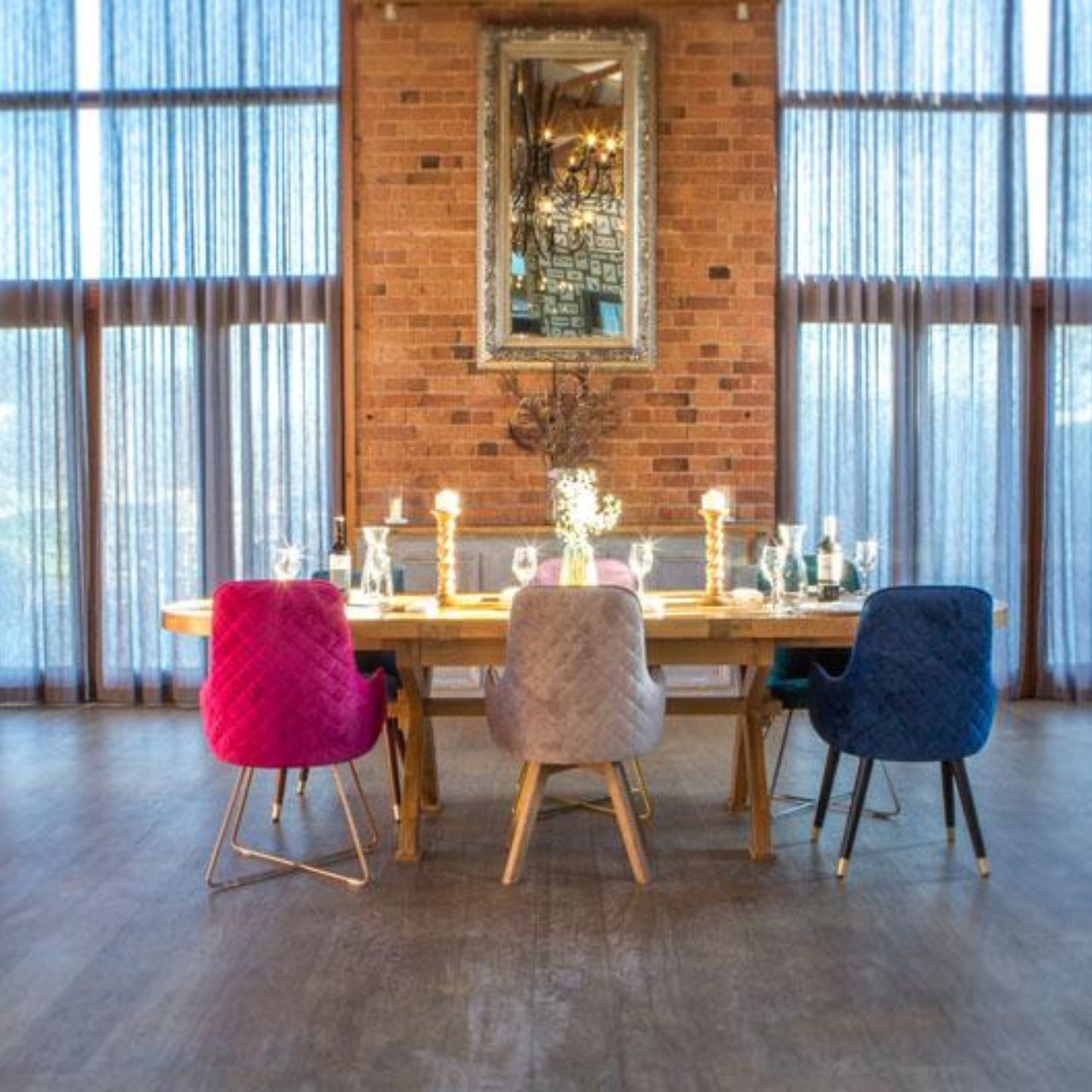 Dining area with a long wooden table and colorful chairs against a brick wall.
