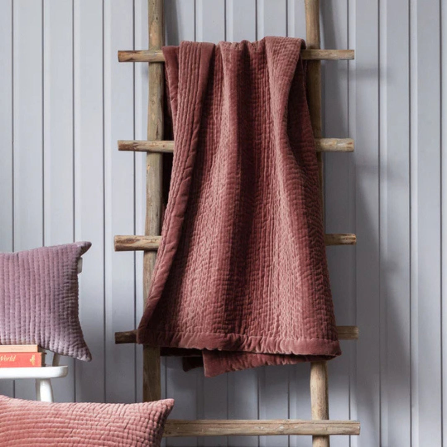 Brown textured blanket draped over a wooden ladder against a gray wall.