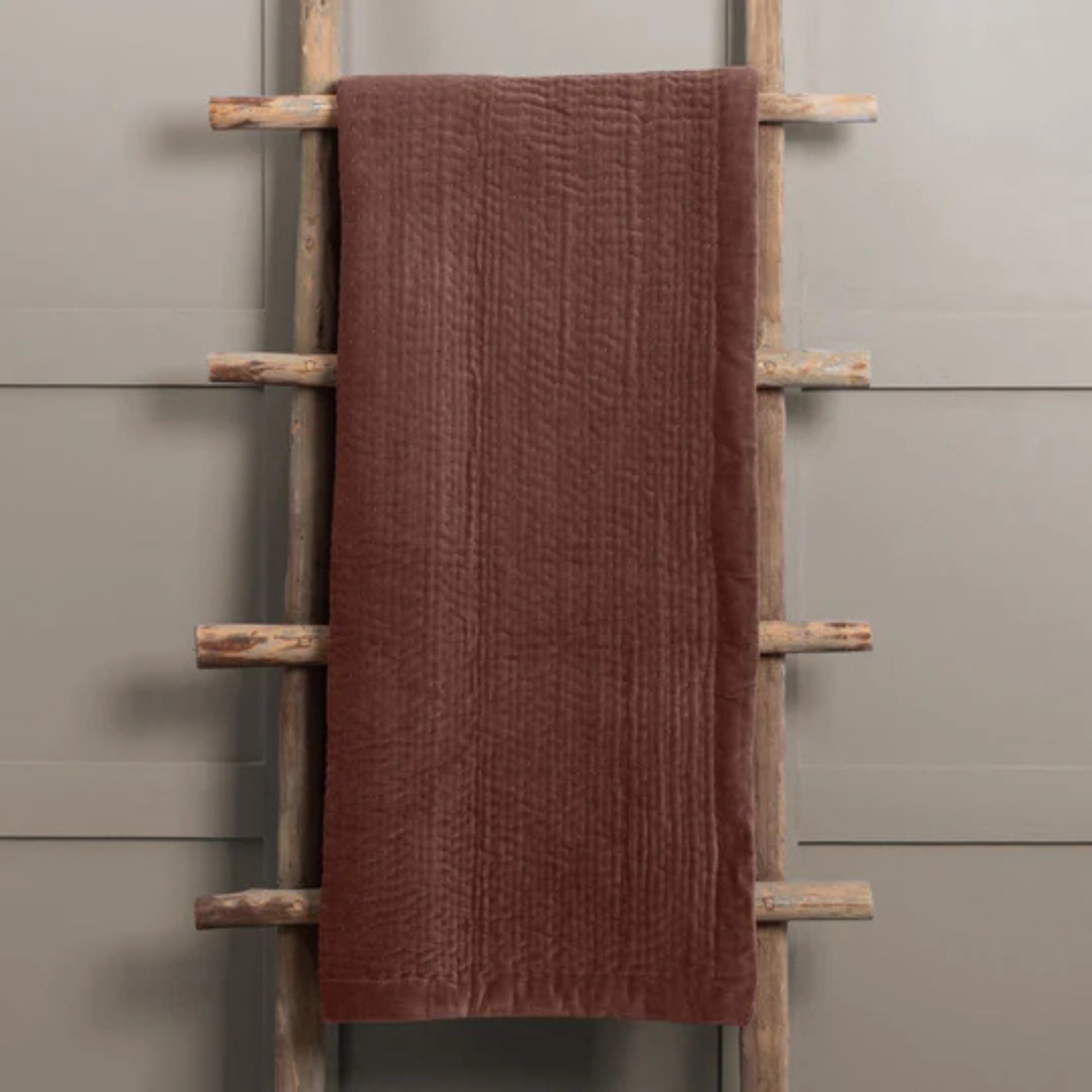 Brown towel draped over a wooden towel rack against a gray wall.