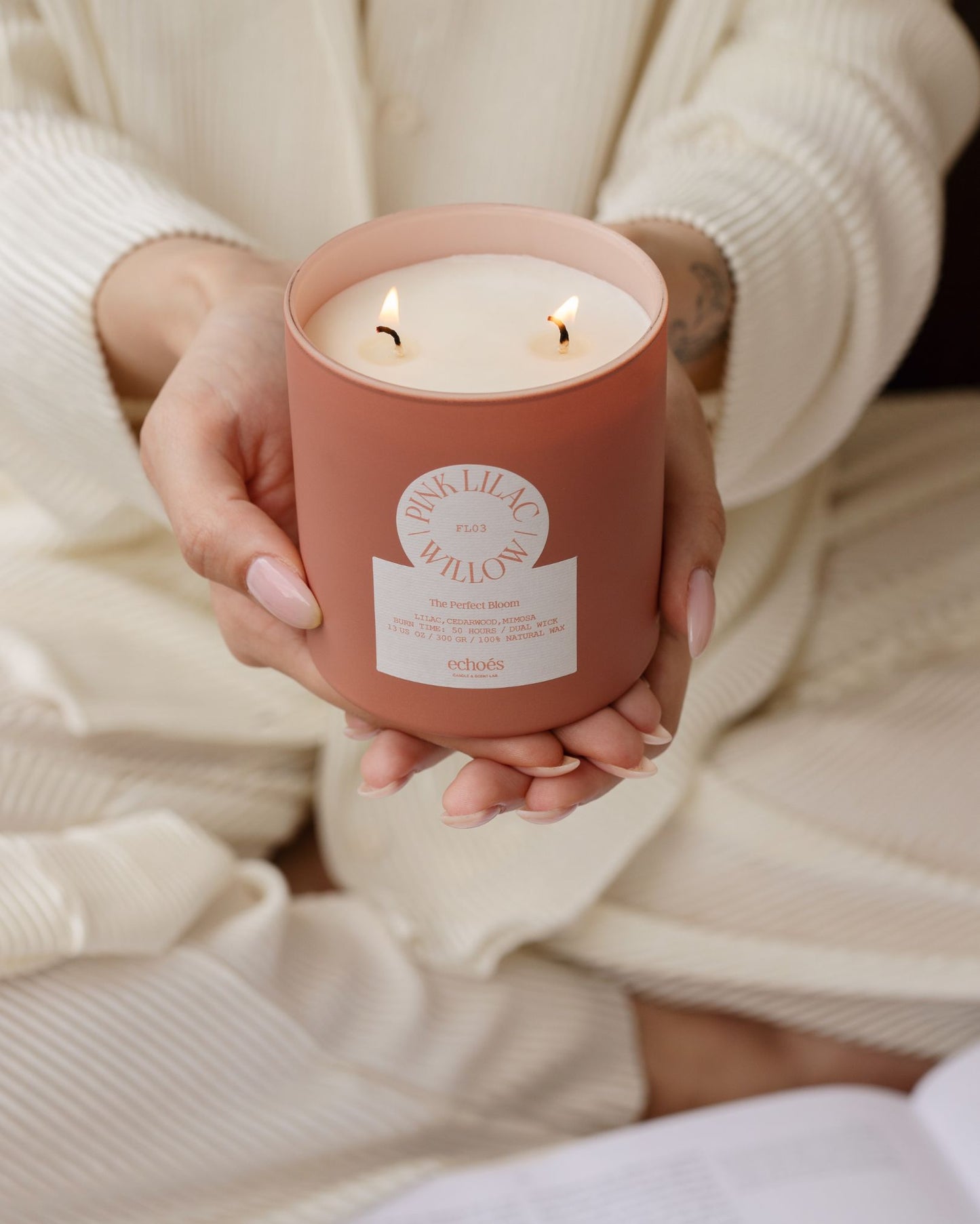 A person holding a pink and lilac colored candle with two wicks, in a jar.