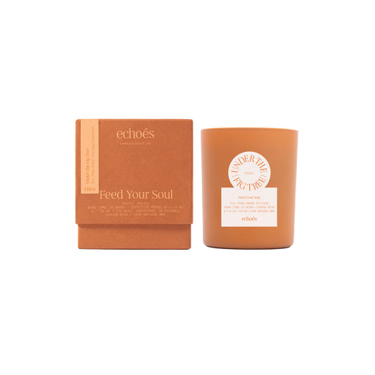 A tumbler candle with a beige label under the fig tree branding, next to its brown packaging box.