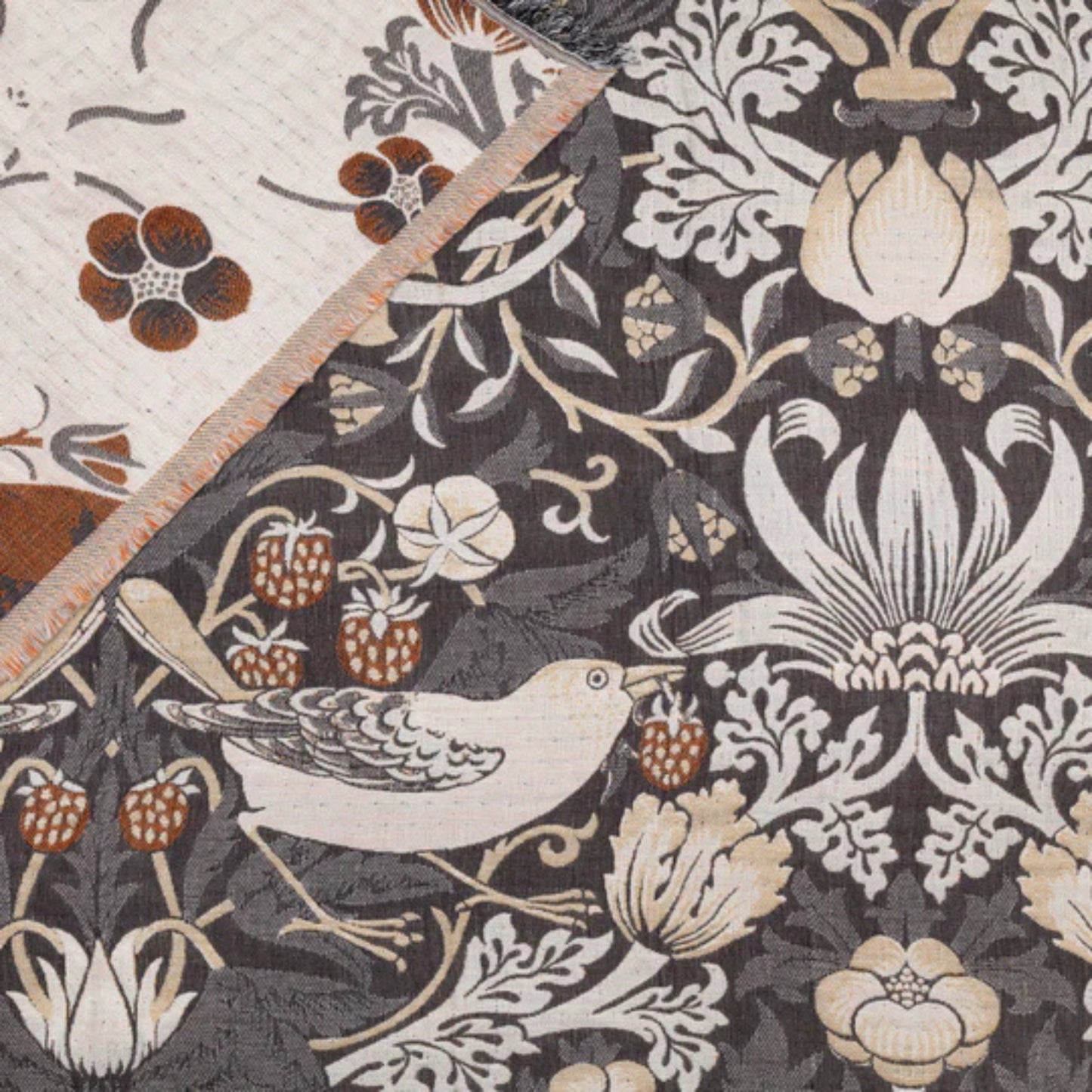 Open throw featuring a floral and bird pattern in biscuit tones on a dark fabric background with a reverse side corner folded back showing lighter colours