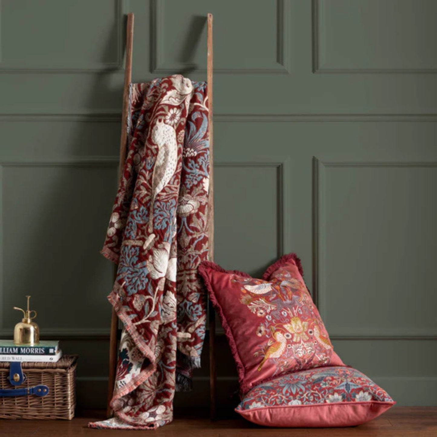 Decorative blanket and pillows with floral patterns on a wooden ladder against a green paneled wall.