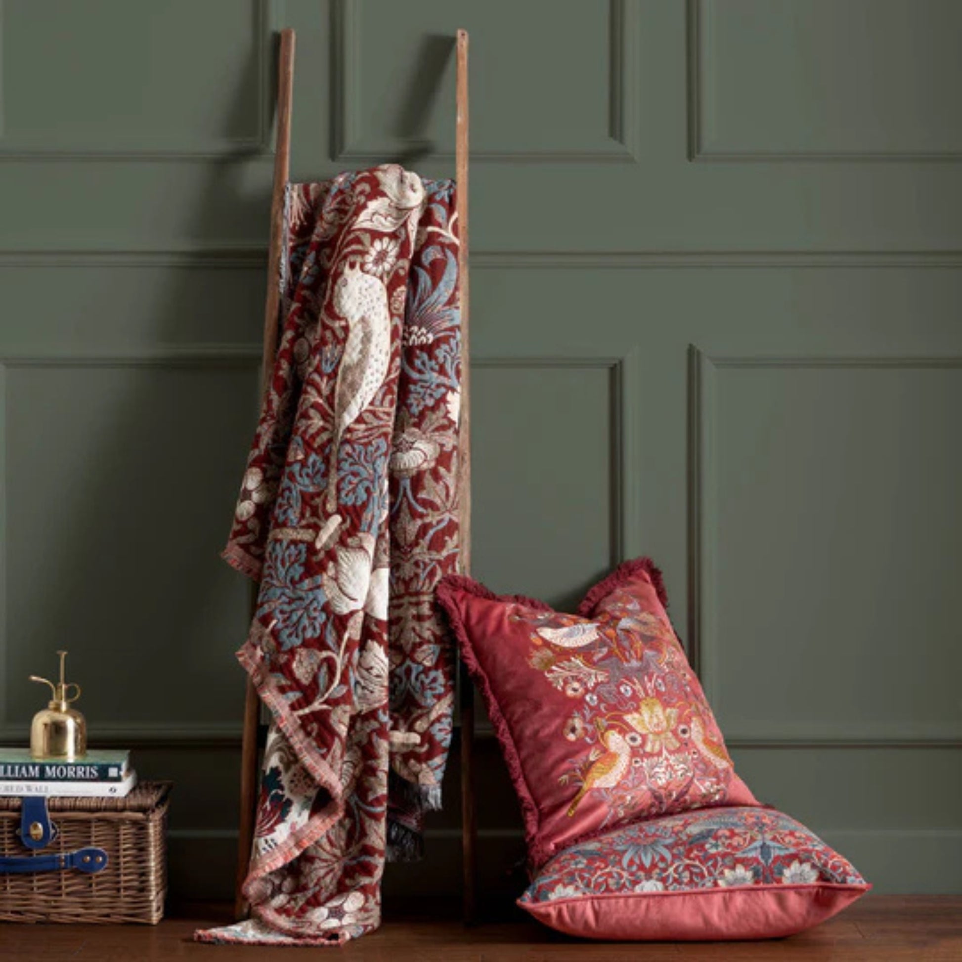 Decorative blanket and pillows with floral patterns on a wooden ladder against a green paneled wall.
