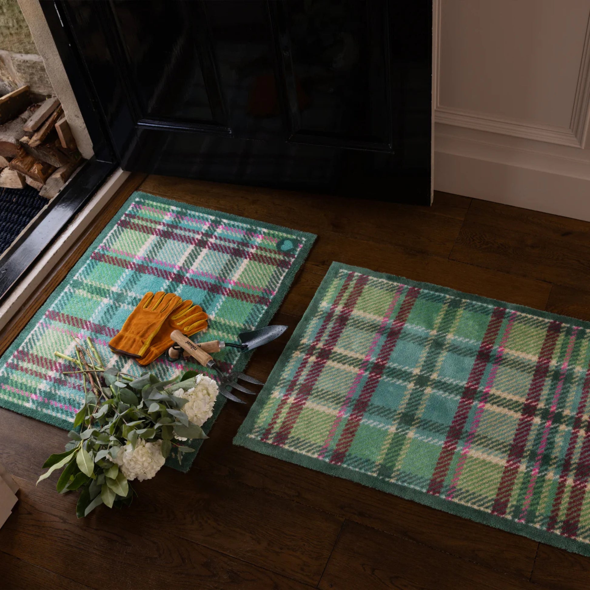 Two plaid mats on a wooden floor with gardening tools and flowers.