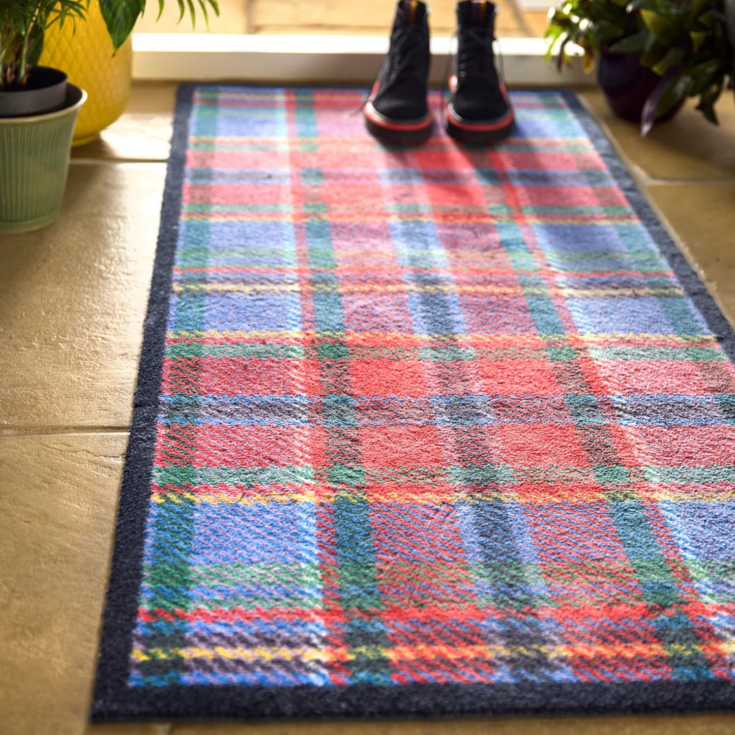 Ble and red tartan hug rug runner mat at entry way with black boots and potted plants