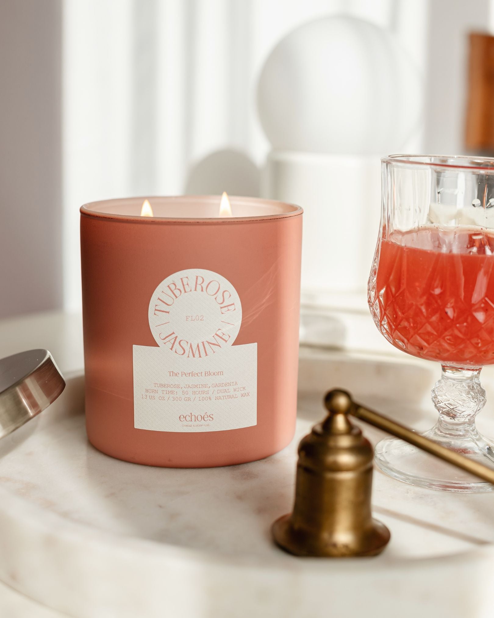 A pink, cylindrical, two-wick candle with the scent of tuberose and jasmine, placed on a marble surface with a reflection of light on its surface.