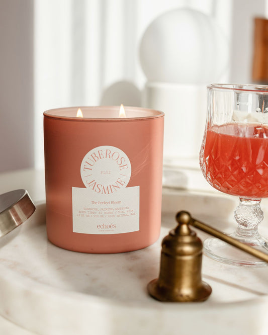 A pink, cylindrical, two-wick candle with the scent of tuberose and jasmine, placed on a marble surface with a reflection of light on its surface.