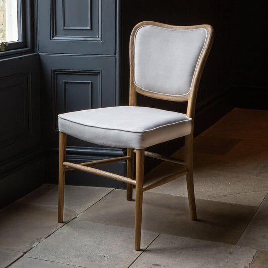 Cream and wood dining chair facing towards a window 