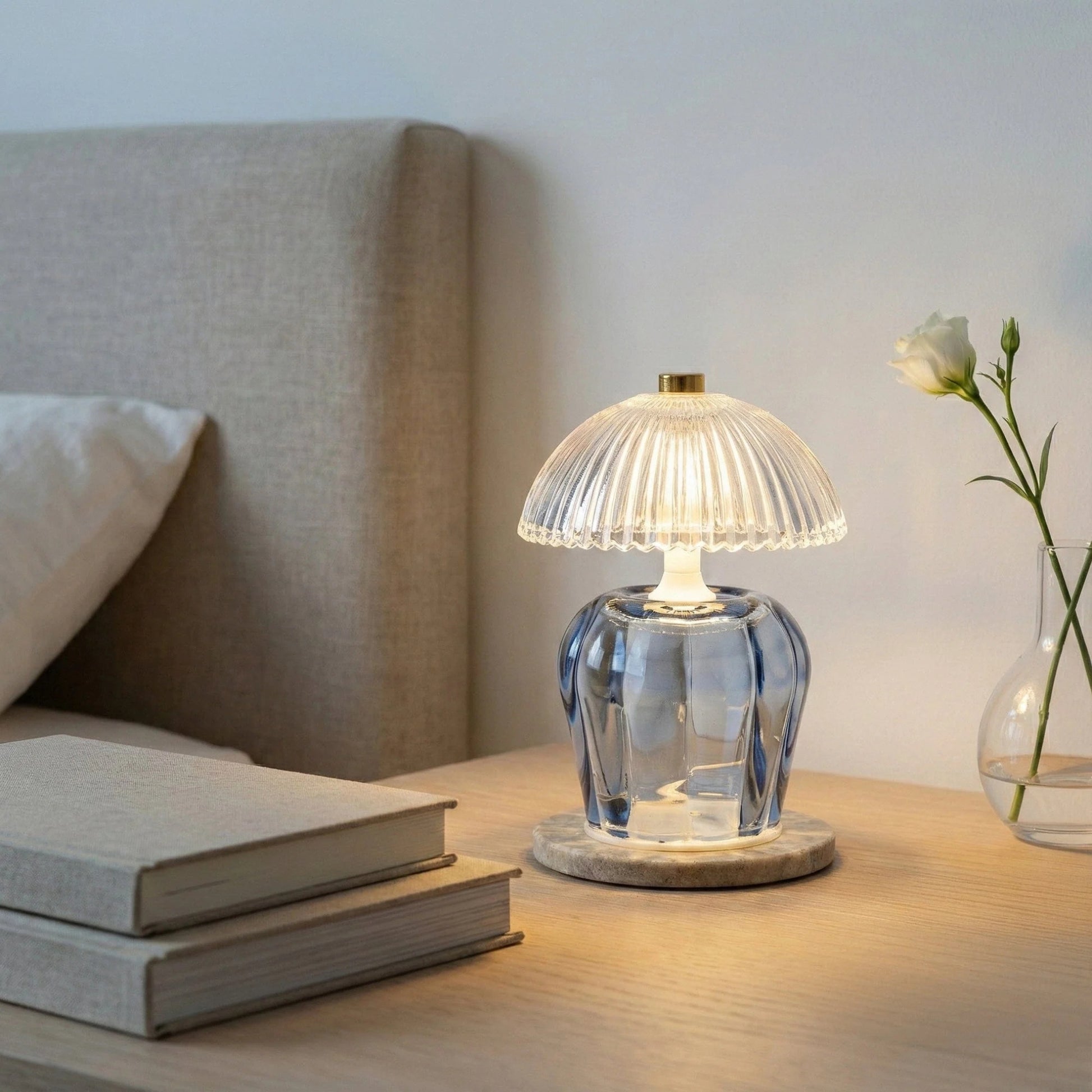 Clear glass table lamp on a wooden surface with books and a vase in the background