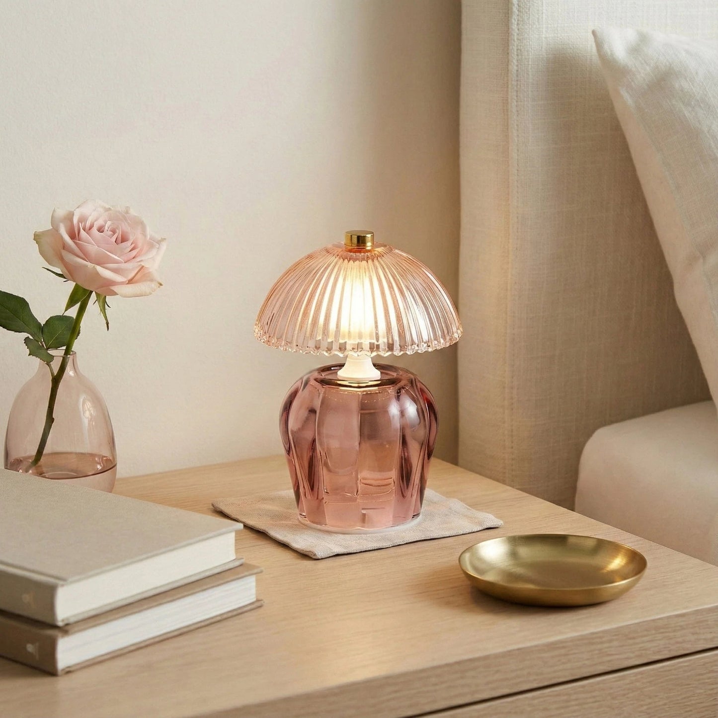 Pink glass table lamp on a wooden surface with books and a vase in the background