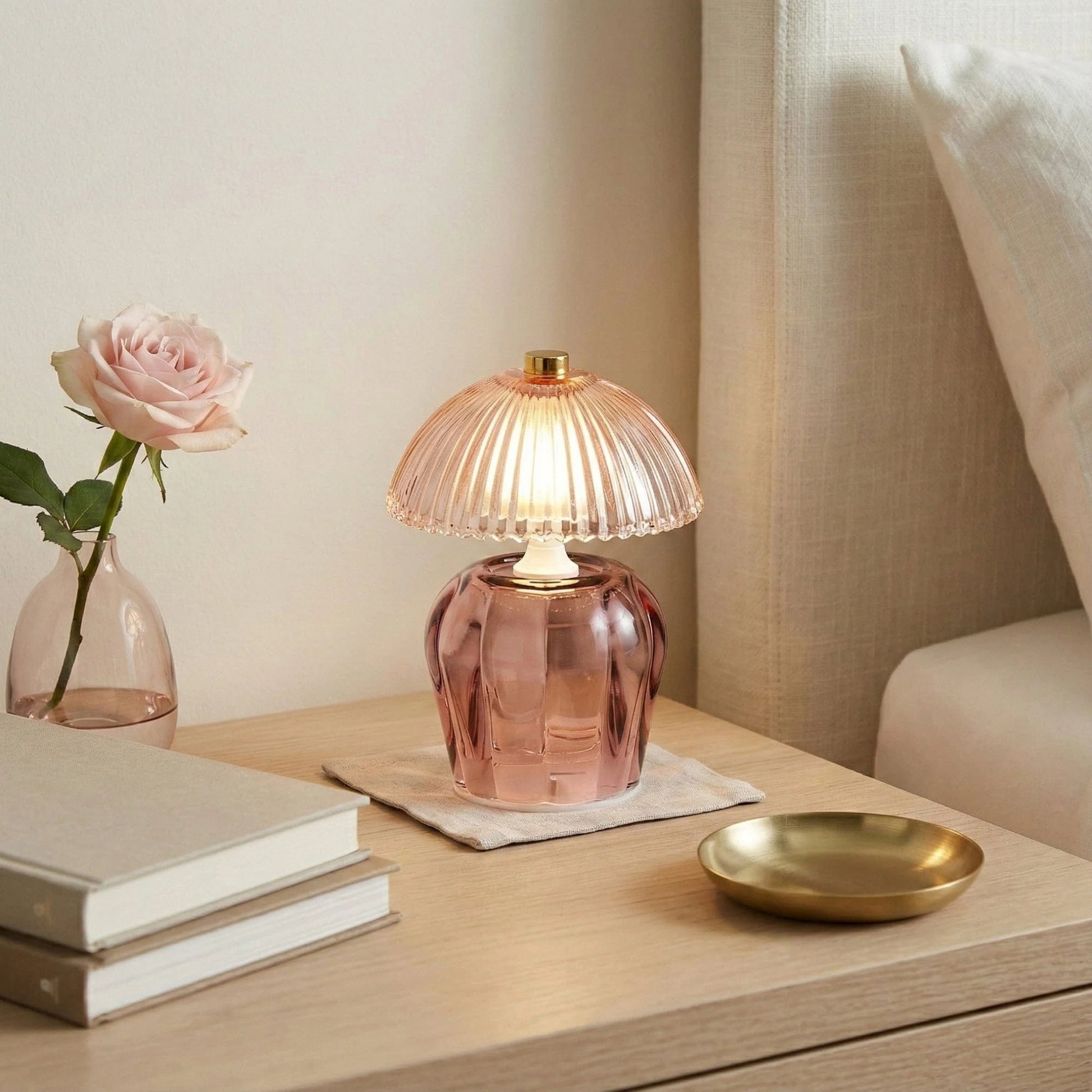 Pink glass table lamp on a wooden surface with books and a vase in the background
