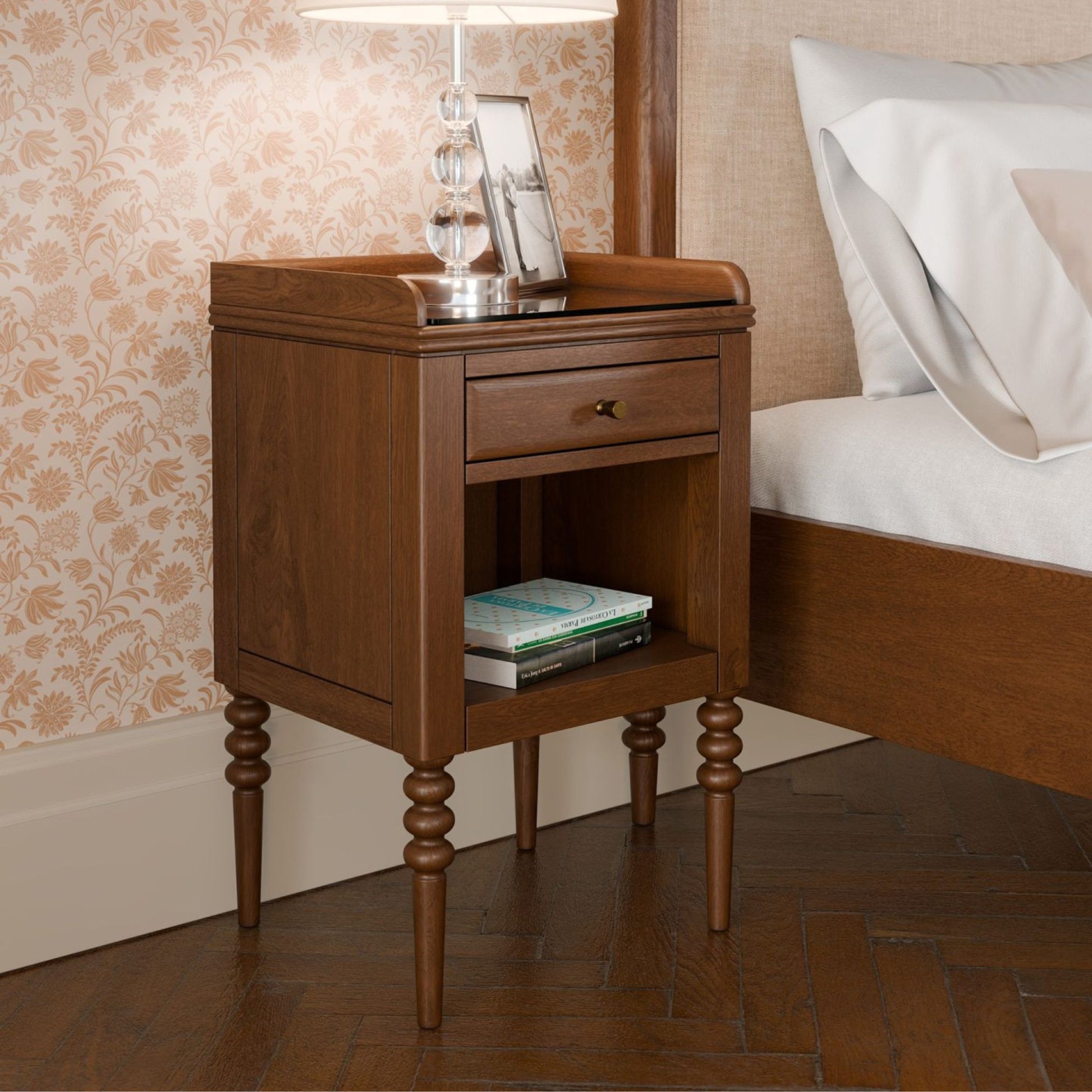 Wooden nightstand with a lamp and books in a bedroom setting