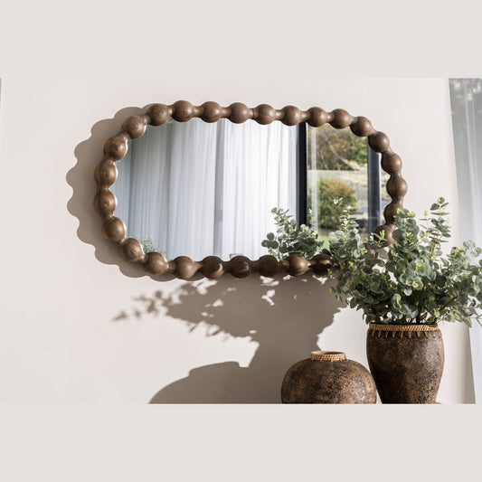 Round wooden-framed mirror on a wall with decorative vases and plants below.